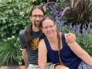 Eva and Rafael in front of colorful flowers and bushes.